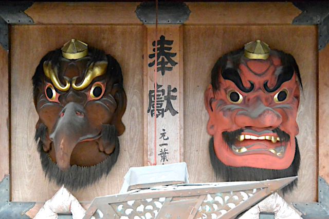 賽銭箱の上の二つの天狗の面